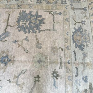 K&ouml;nnte beinhalten: Ein gro&szlig;er, rechteckiger Teppich mit einem aufwendigen, traditionellen Design. Der Teppich hat einen cremefarbenen Hintergrund mit einem sich wiederholenden Muster aus blauen, gr&uuml;nen und beigen floralen und geometrischen Motiven. Der Rand ist in einem dunkleren Blau- und Beigeton gehalten.