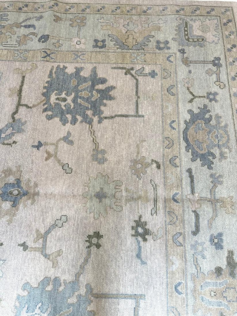 K&ouml;nnte beinhalten: Ein gro&szlig;er, rechteckiger Teppich mit einem aufwendigen, traditionellen Design. Der Teppich hat einen cremefarbenen Hintergrund mit einem sich wiederholenden Muster aus blauen, gr&uuml;nen und beigen floralen und geometrischen Motiven. Der Rand ist in einem dunkleren Blau- und Beigeton gehalten.
