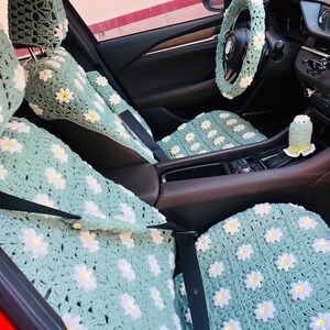 May include: Crocheted car seat covers, steering wheel cover, and accessories in a light green color with white and yellow daisy flower accents. The interior of the car is visible, showcasing the custom-made, decorative items.