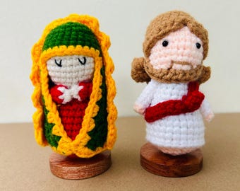 May include: Two handmade crochet religious figures. One figure is dressed in red, green, and yellow, and the other is in white with a red sash. Both figures are on small wooden bases.