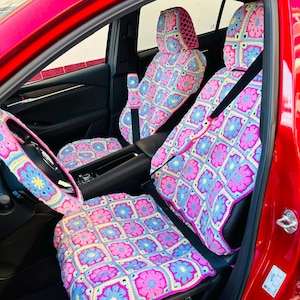 Puede incluir: Interior de coche con un vibrante juego de ganchillo hecho a mano. El juego incluye fundas de asiento, fundas de reposacabezas, una funda de volante y una funda de consola central. El diseño de ganchillo presenta patrones florales rosas, azules y amarillos.
