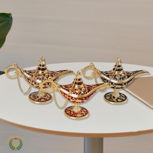 May include: Three decorative genie lamps in red, gold, and black. Each lamp features ornate detailing, a curved spout, and a handle with a chain. The lamps are displayed on a white table.