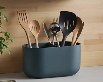 Può includere: Un portautensili teal pieno di vari utensili da cucina. Gli utensili includono spatole e cucchiai di legno, una spatola nera, un mestolo di metallo, una forchetta e un coltello. Il portautensili è su una superficie bianca con uno sfondo di legno.