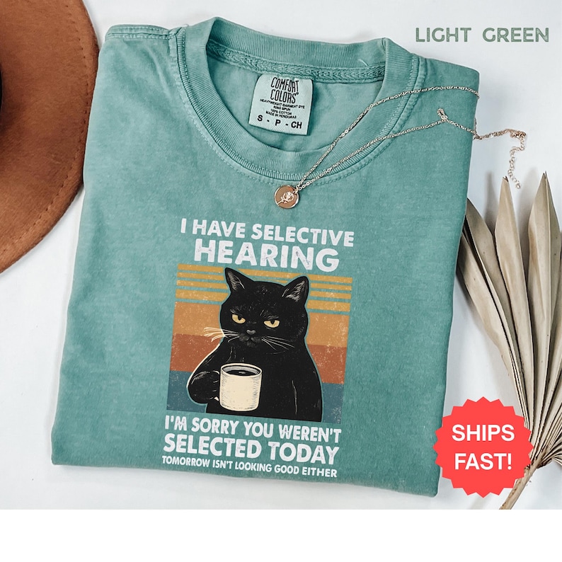 May include: Light green t-shirt with the text "I HAVE SELECTIVE HEARING" and a graphic of a black cat holding a mug. The shirt also has the text "I'M SORRY YOU WEREN'T SELECTED TODAY" and "TOMORROW ISN'T LOOKING GOOD EITHER".