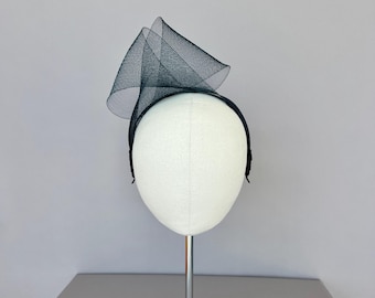 May include: Black mesh headband with a large, folded, cone-shaped design. The headband is displayed on a white mannequin head.