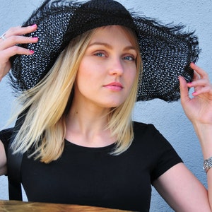 K&ouml;nnte beinhalten: Eine Frau mit blonden Haaren tr&auml;gt einen schwarzen breitkrempigen Sonnenhut mit einem schwarz-wei&szlig;en Muster. Sie tr&auml;gt ein schwarzes, kurz&auml;rmeliges Hemd.