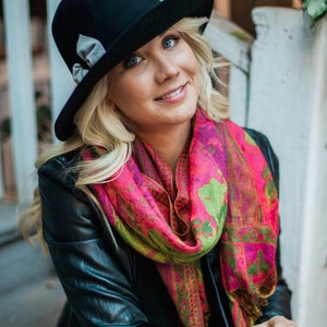 Peut inclure: Une femme portant un fedora noir avec un ruban gris, une veste en cuir noir et une &eacute;charpe &agrave; motifs rose et vert.