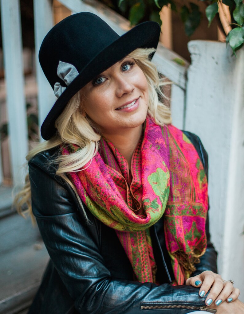 Peut inclure: Une femme portant un fedora noir avec un ruban gris, une veste en cuir noir et une &eacute;charpe &agrave; motifs rose et vert.