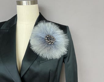 May include: A gray blazer with a light blue fur brooch with a silver and black rhinestone center.