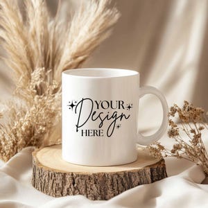 May include: A white ceramic mug with a handle, featuring the text "YOUR Design HERE" in a stylish script. The mug sits on a rustic wooden slice, with dried plants in the background. Ideal for custom designs.
