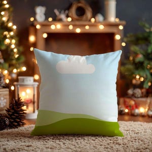 May include: Square cushion featuring a sky blue design with a white cloud and green hills. The cushion is placed on a brown rug, with a Christmas tree and fairy lights in the background.