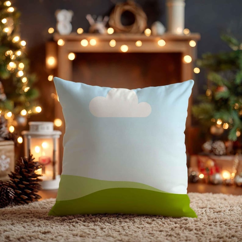 May include: Square cushion featuring a sky blue design with a white cloud and green hills. The cushion is placed on a brown rug, with a Christmas tree and fairy lights in the background.
