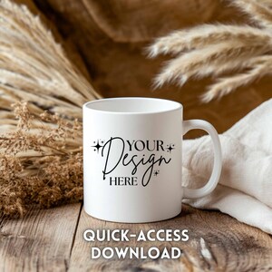 May include: A white ceramic mug with a curved handle. The mug features the text "YOUR Design HERE" in a stylish script font, with the words "QUICK-ACCESS DOWNLOAD" below. The mug is set on a wooden surface with dried plants in the background.