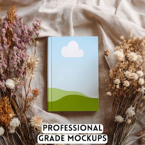 May include: A hardcover book with a sky blue cover featuring a white cloud and green hills. The book is surrounded by dried flowers and the text "PROFESSIONAL GRADE MOCKUPS" is at the bottom.