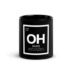 Puede incluir: Una taza de cerámica negra con un gráfico cuadrado blanco. El gráfico presenta el número "17" en la parte superior, las letras "OH" en fuente grande y la palabra "OHIO" debajo, junto con las coordenadas de latitud y longitud.