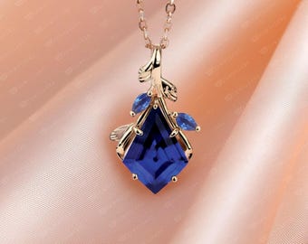 May include: A gold-toned necklace with a pendant featuring a large, faceted, deep blue gemstone in a diamond shape. The pendant is accented with smaller blue gemstones and leaf-like details. The chain is delicate.