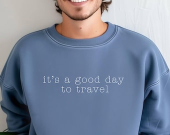 Könnte beinhalten: Blaues Sweatshirt mit Rundhalsausschnitt und dem weißen Aufdruck "it's a good day to travel". Das Sweatshirt ist einfarbig und hat ein schlichtes, klassisches Design, das sich für Freizeitkleidung eignet.