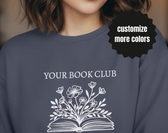 May include: A slate blue sweatshirt with the text "YOUR BOOK CLUB" above a white floral design emerging from an open book. Below the design is the text "MY WEEKEND IS FULLY BOOKED". A black starburst graphic reads "customize more colors".