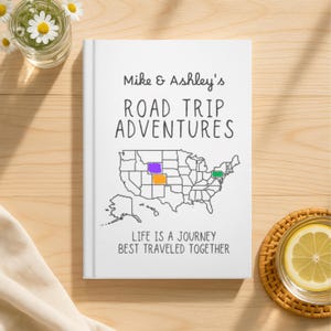 May include: A white hardback journal with the title "Mike & Ashley's Road Trip Adventures." The cover shows a map of the USA with highlighted states and the words "Life is a journey best traveled together."