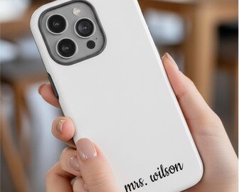 May include: A white smartphone case with a black camera module and the text "mrs. wilson" in black script. The case has a smooth, glossy finish. The phone case is held in a person's hand. The case is designed to fit a smartphone.