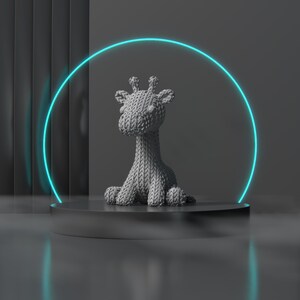 May include: A grey knitted giraffe ornament sits on a dark grey platform, lit by a neon blue halo. The giraffe has a textured appearance, with visible knit detailing. The background is a gradient of dark grey.