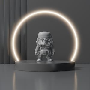 Puede incluir: Una figura gris de Stormtrooper se encuentra sobre una plataforma circular gris oscuro, iluminada por un anillo brillante. La figura tiene detalles de armadura y casco. El fondo es un degradado de tonos grises.