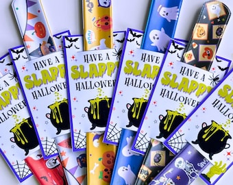 May include: A collection of Halloween-themed slap bracelets with matching cards. The bracelets feature various spooky designs, including ghosts, pumpkins, and skeletons. The cards read "Have a Slappy Halloween" with a cauldron graphic. Decorative bats, spiders, and witch hats surround the bracelets.