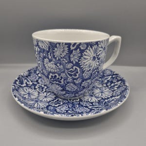 May include: A ceramic teacup and matching saucer featuring a deep blue and white floral pattern. The design consists of intricate, repeating chrysanthemum-like flowers and leafy foliage covering the entire exterior of the cup and the saucer surface.