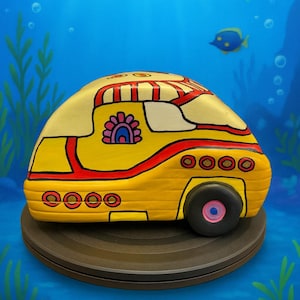 May include: A yellow submarine-shaped decorative object with red and white accents. The toy has a black wheel with a pink center and is set against a blue background with fish and bubbles.