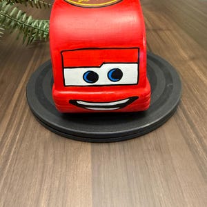 May include: A red, rectangular, hand-painted decorative item resembling a cartoon car. It features a white rectangle with blue eyes and a smiling mouth. The top has the text "Dust EZE Medicated" in a yellow oval.