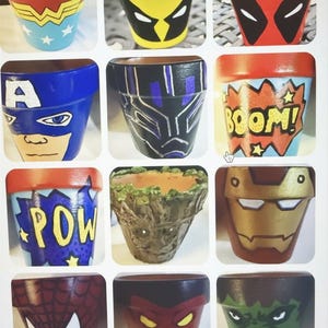 May include: A collection of hand-painted terracotta flower pots featuring superhero and comic book character designs. The pots showcase characters like Wonder Woman, Deadpool, Captain America, Black Panther, and others, with vibrant colors and detailed artwork. Each pot is a unique piece of art.