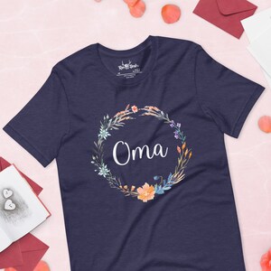Puede incluir: Camiseta azul marino con un diseño de corona de flores y la palabra "Oma" en letras blancas.