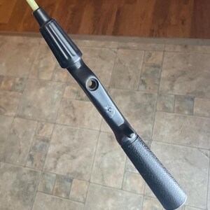 May include: A black tool with a textured handle and a light green rod extending from the top. The tool has a cylindrical shape with a hole near the center and a ridged section near the top.