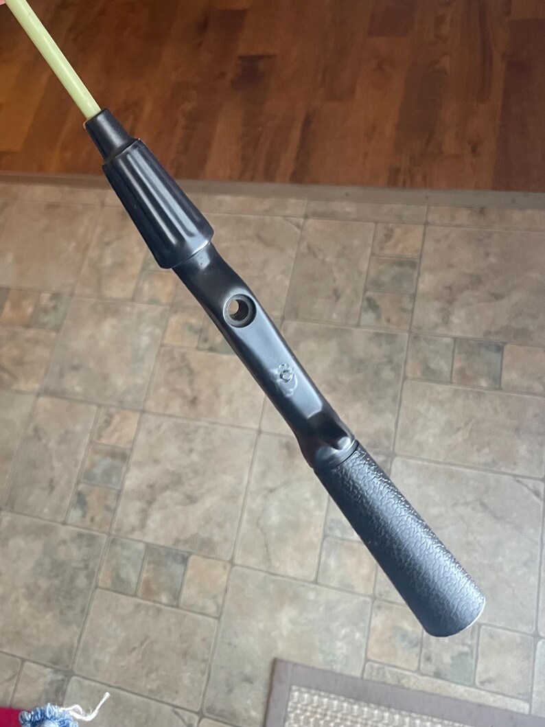 May include: A black tool with a textured handle and a light green rod extending from the top. The tool has a cylindrical shape with a hole near the center and a ridged section near the top.