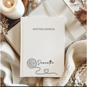May include: A white Knitting Journal with the name "Samantha" and a yarn ball design. The journal's cover features the text "KNITTING JOURNAL" in a simple, elegant font. The journal is surrounded by a cozy, neutral-toned aesthetic with a candle and a knitted item.