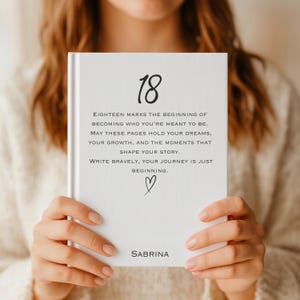May include: A white journal with the number "18" and the name "Sabrina" printed on the cover. The journal includes inspirational text about dreams and growth. A small heart is drawn below the text.