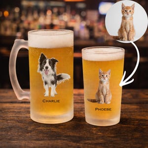 May include: Two frosted beer glasses filled with beer. One glass features a black and white dog graphic with the name "Charlie". The other glass has an orange kitten graphic with the name "Phoebe". A photo of the kitten is in the background.