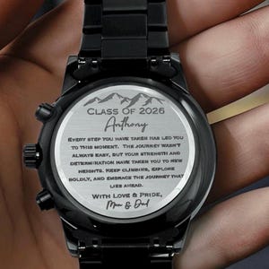 May include: A black wristwatch with a metal band. The watch face features the text "CLASS OF 2026" and "Anthony", along with an inspirational message. The watch is held in a hand.