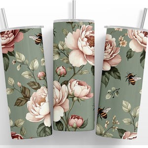 May include: A set of three stainless steel tumblers with floral and bee designs. The tumblers feature a light green background with pink and white flowers, green leaves, and illustrations of bees. Each tumbler has a silver lid and a silver straw.