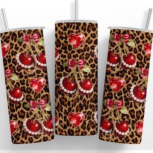 May include: Three stainless steel tumblers with a leopard print design. Each tumbler features a pattern of red cherries, heart-shaped gems, and gold chains. The cherries are adorned with pearls and red bows.