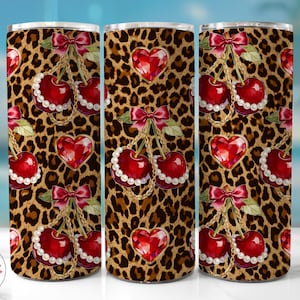 Puede incluir: Un vaso con un fondo de estampado de leopardo con cerezas rojas adornadas con perlas y lazos, junto con gemas en forma de corazón. El diseño incluye cadenas doradas y un logotipo de cereza.