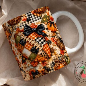May include: A white ceramic mug featuring a colourful autumn-themed pattern with a central football graphic adorned with a black bow. The design includes orange, yellow, and green fall leaves, pumpkins, leopard print, and black and white buffalo plaid.