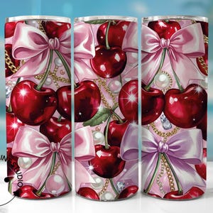 May include: A tumbler featuring a repeating pattern of glossy red cherries, pink bows, gold chains, and pearls on a light pink background. The design includes sparkling diamond accents. The tumbler has a cylindrical shape.