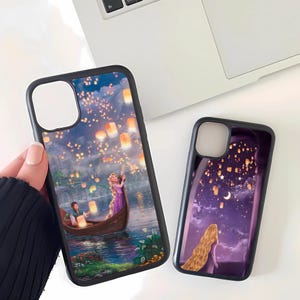 May include: Two black phone cases with colorful illustrations. One case depicts a boat scene with floating lanterns, a woman in a purple dress, and a man. The other case shows a woman with long blonde hair looking at floating lanterns.