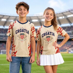 A young boy and girl wearing matching Croatia soccer jerseys stand together on a soccer field.