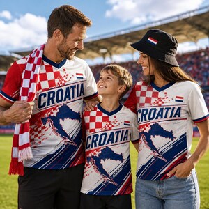 A man, woman, and child wearing Croatia national team jerseys and a red and white scarf are standing together on a sports field.