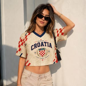A woman wearing a Croatia jersey and sunglasses stands against a white wall, with her hand on her head.