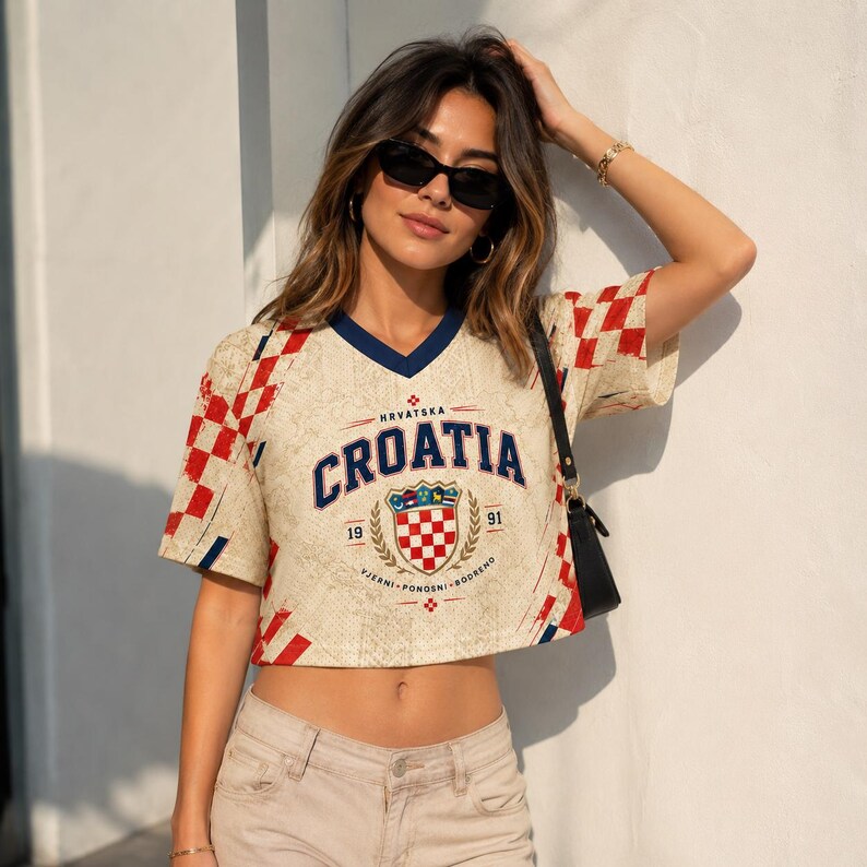 A woman wearing a Croatia jersey and sunglasses stands against a white wall, with her hand on her head.