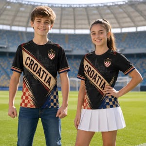A young boy and girl wearing matching black and red striped jerseys with the word "Croatia" printed on them, standing on a soccer field.