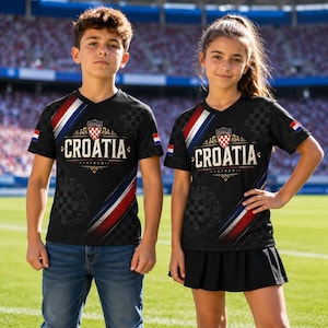 Two children wearing black t-shirts with red, white, and blue stripes and the word "Croatia" printed on them, standing on a soccer field.